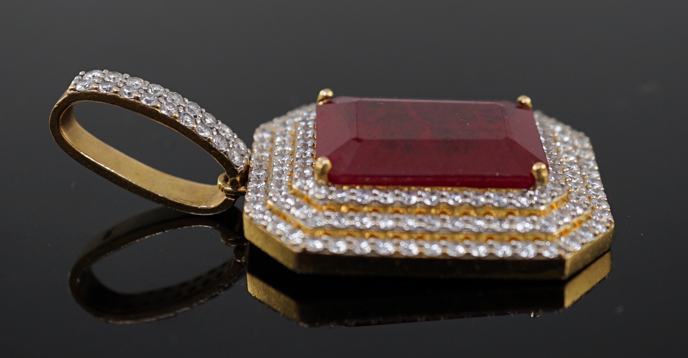 A large modern 18ct gold and single emerald cut synthetic ruby set pendant, bordered by three concentric bands of round brilliant cut diamonds